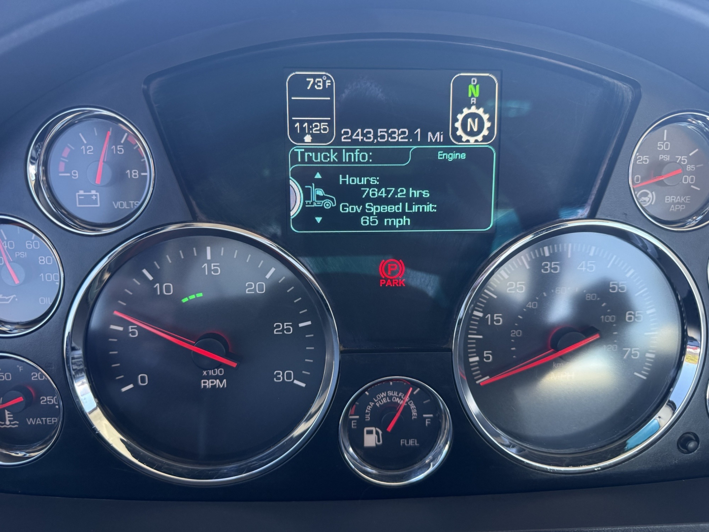 Dashboard of a Kenworth T680 showing digital truck info display with hours, mph, and engine data, surrounded by analog gauges.