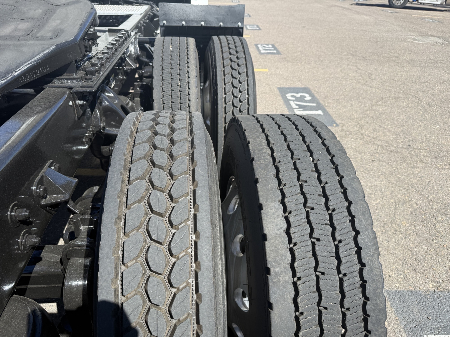Kenworth T680 wheelview showing dual rear axles with treaded tires and chassis components in a truck yard.