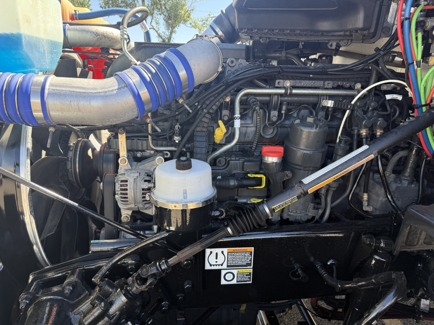 Kenworth T680 engine bay showing intake tubing, hydraulic lines, and engine components.
