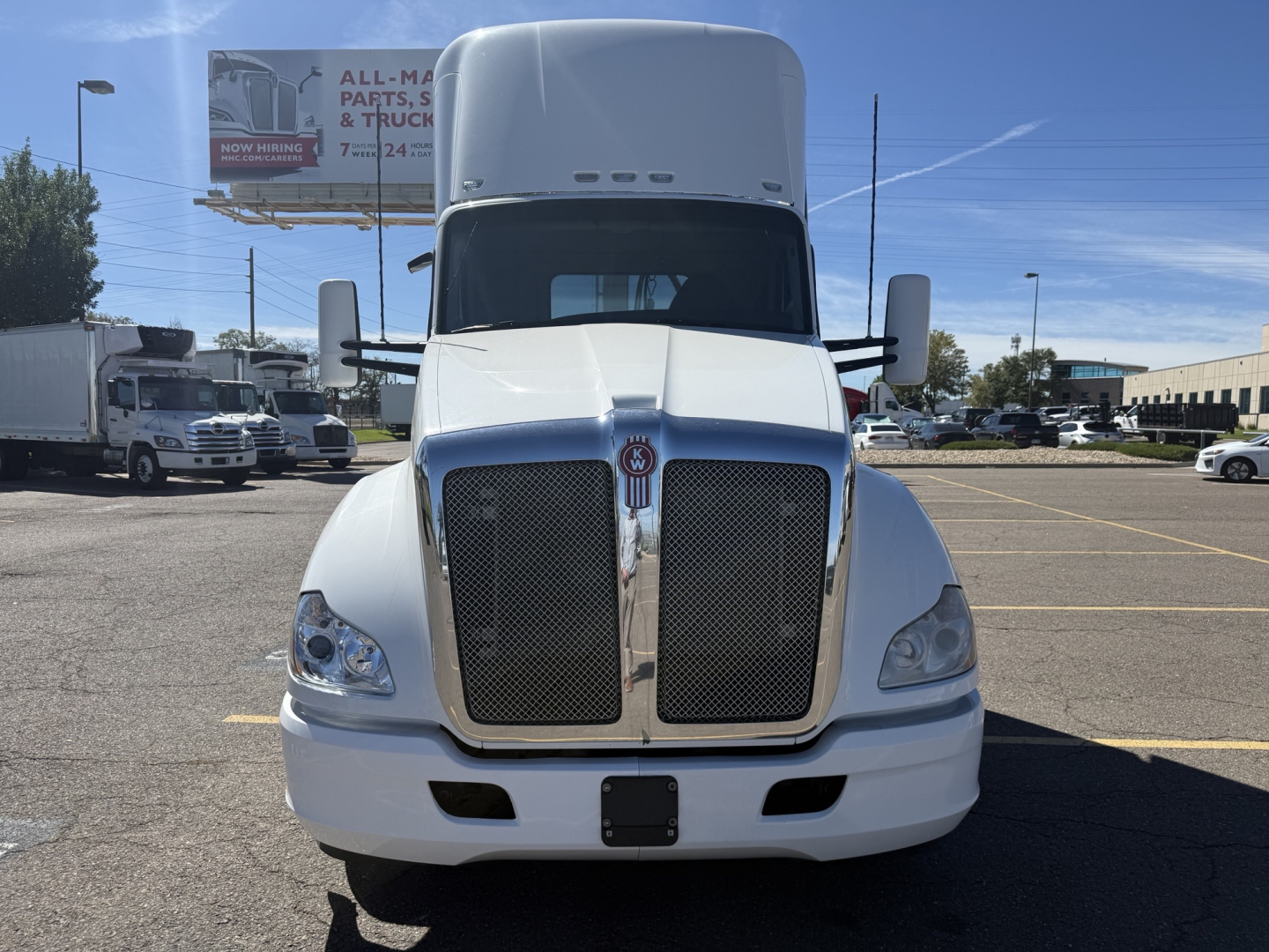 Kenworth T680 front view showing large black grille with chrome surround and white body in a parking lot.