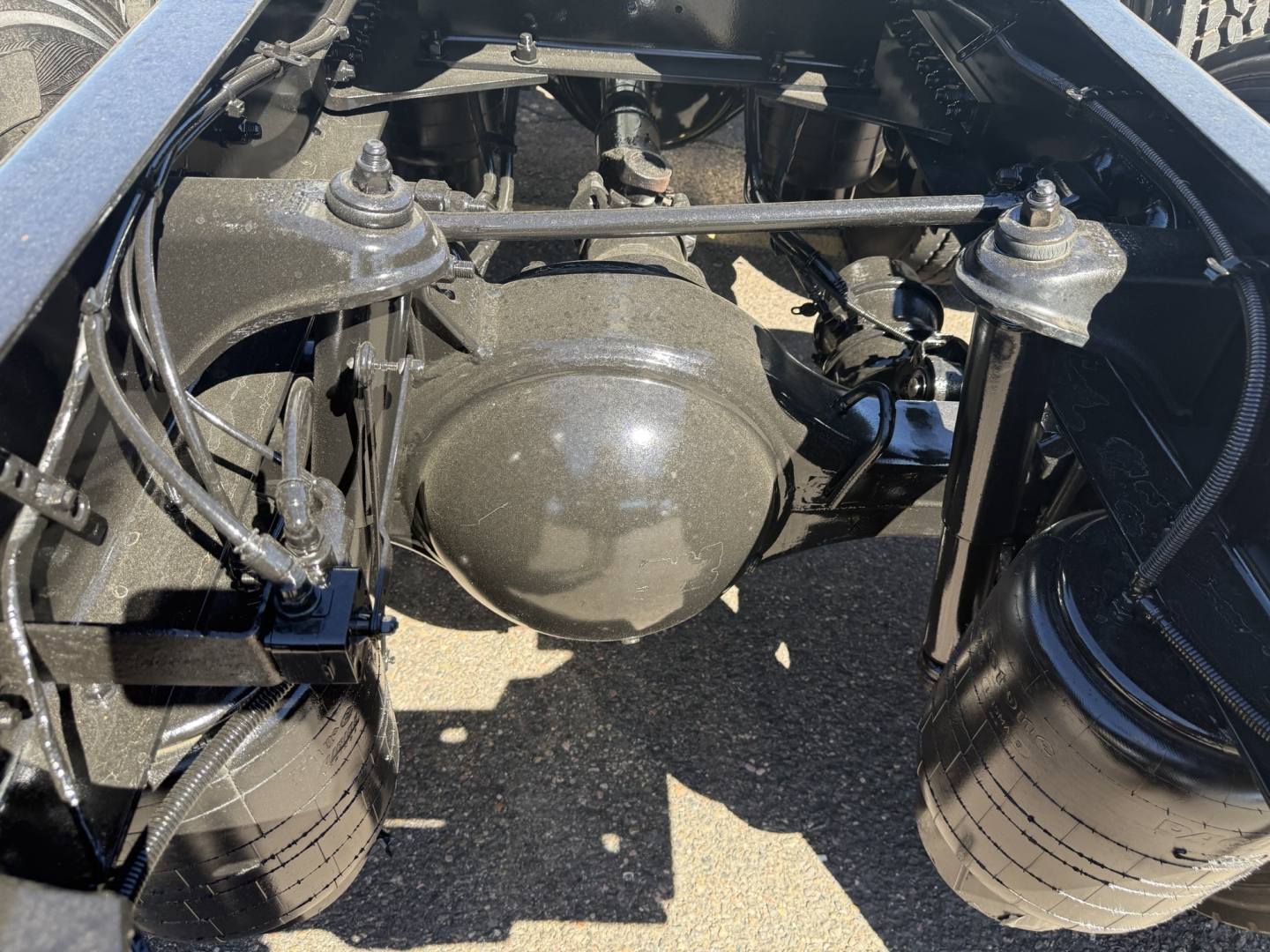 Kenworth T680 rear suspension/hub area showing axle housing, air lines, and framing; view of driveline components and fuel/air lines in engine bay area.