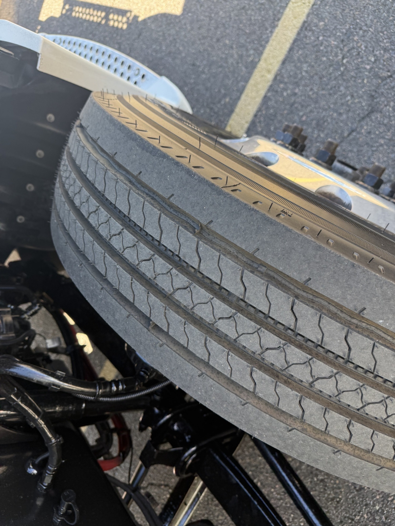 Kenworth T680 wheel and front fender with tire tread and chassis components visible.