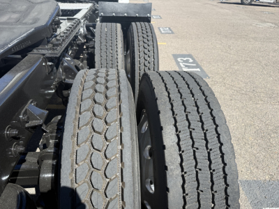 Kenworth T680 wheelview showing dual rear axles with treaded tires and chassis components in a truck yard.