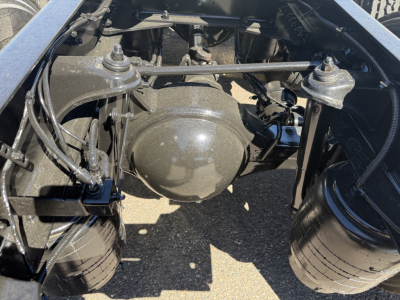 Kenworth T680 rear suspension/hub area showing axle housing, air lines, and framing; view of driveline components and fuel/air lines in engine bay area.