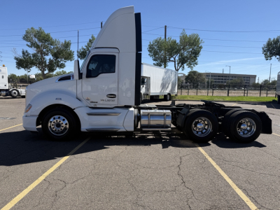 Kenworth T680 tractor side profile with sleeper cab, white paint, chrome fuel tanks, and dual rear axles in a parking lot.