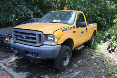 Ford F-250 Super Duty pickup truck in park ranger livery, yellow body, black front grille, side lettering Park Ranger, in grassy lot.