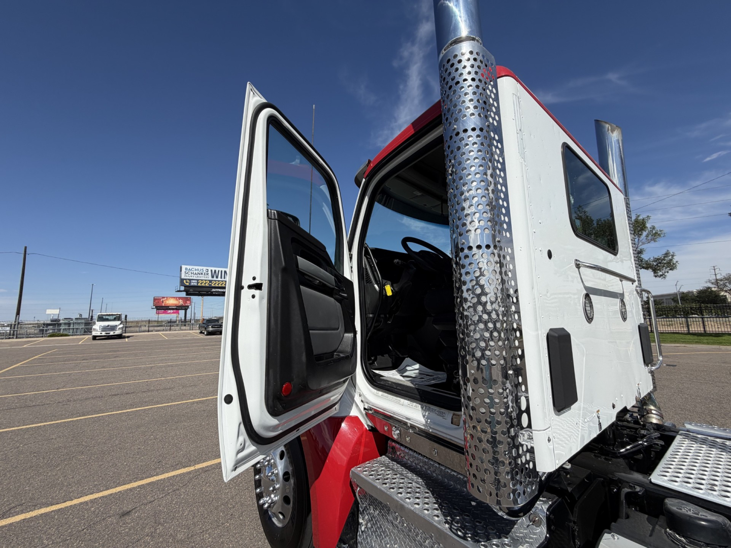 Kenworth T880 cab interior and open door showing driver seat area and chrome exhaust stack, side step, and cab entry with blue sky background.