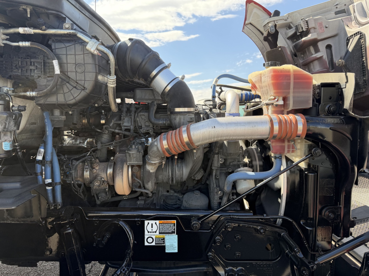 Kenworth T880 engine bay with intake hose, radiator, and hoses visible; warning label on front fender area.