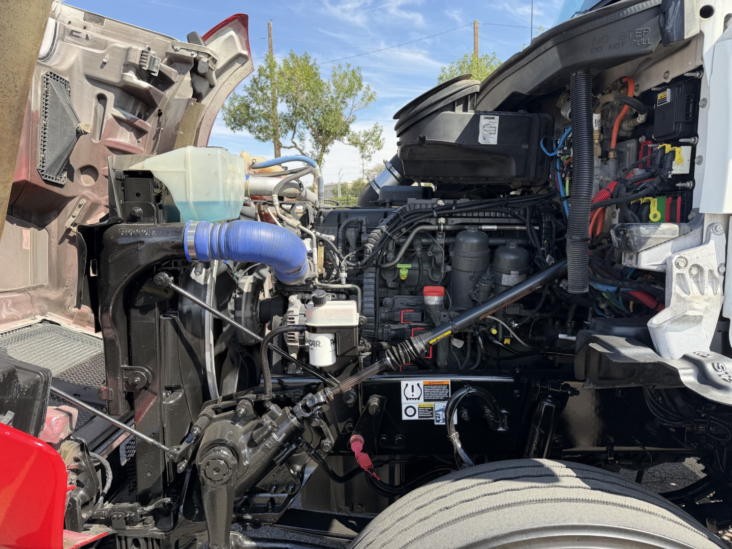 Kenworth T880 engine bay visible with components, hoses, and wiring; front grille area open showing coolant reservoir, hoses, and engine compartments.