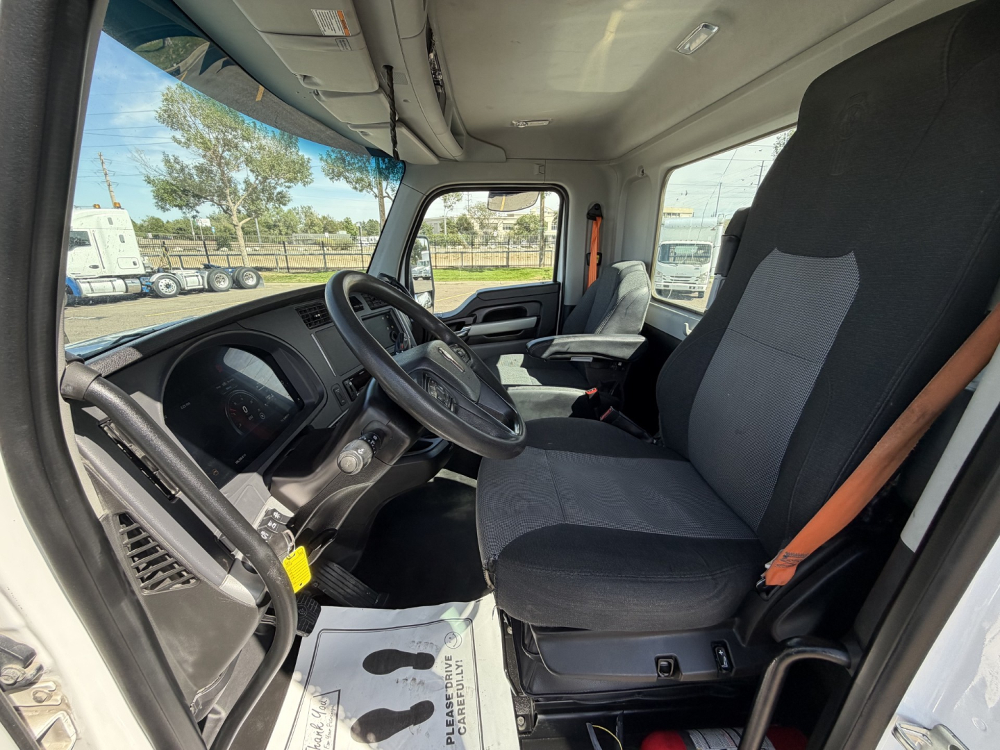 Kenworth T880 interior cab view showing driver seat and steering wheel with dashboard, pedals, and passenger seat in a daycab truck.