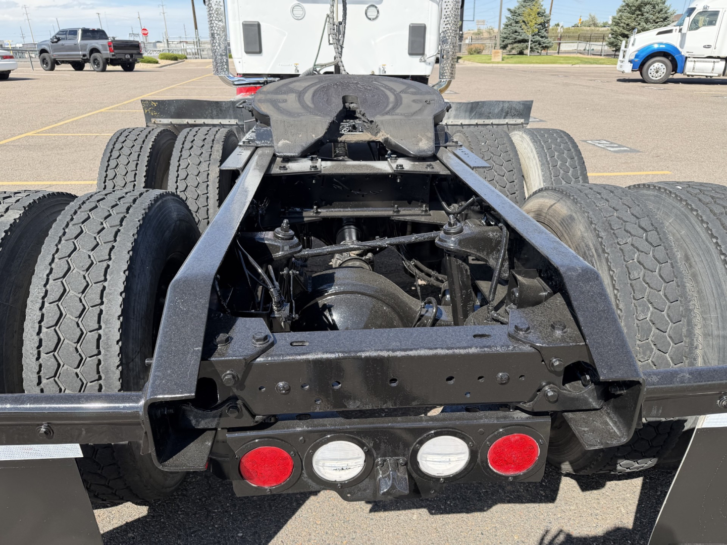 Kenworth T880 center rear chassis showing suspension, driveline, and dual rear axles with tires; proximity view of frame, fifth wheel base, and taillamp lights.
