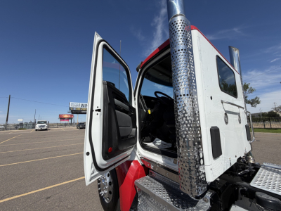 Kenworth T880 cab with open door showing interior seating and chrome vertical exhaust piping; exterior step and door frame visible.