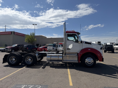 Kenworth T880 conventional daycab tractor in a parking lot side view showing chrome fuel tanks and exhaust stack.