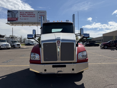 Kenworth T880 front view showing large grille and bumper, truck cab in white and maroon, daytime with dealership lot in background.