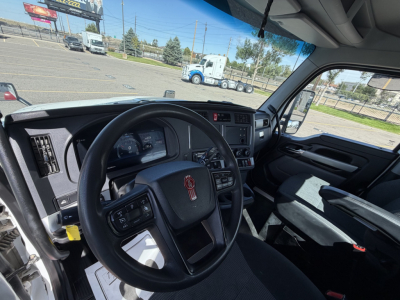 Kenworth T880 interior view showing steering wheel, dashboard, and driver’s seat with large windshield and highway scene outside.