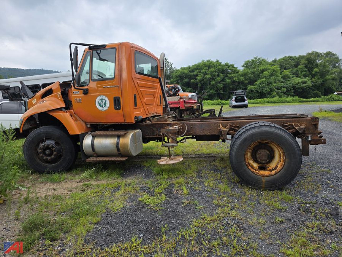 Cab and chassis truck with orange cab, exposed frame rails, large tires, and a badge on the door. Side view showing chassis with empty rear frame and wheel.
