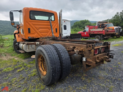 Cab and chassis truck showing rear frame and single rear axle, 2003 International WorkStar 7500, orange cab, exposed drivetrain, rust on frame, Parked in lot.