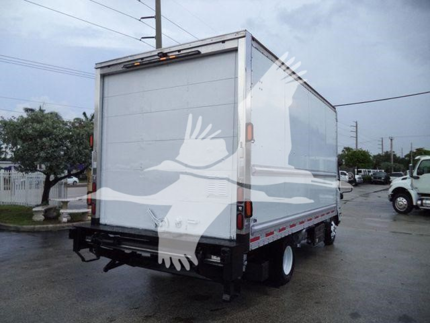 Box truck rear view showing Isuzu NPR-HD style box with plain white doors and black undercarriage, no legible text visible on the vehicle itself.