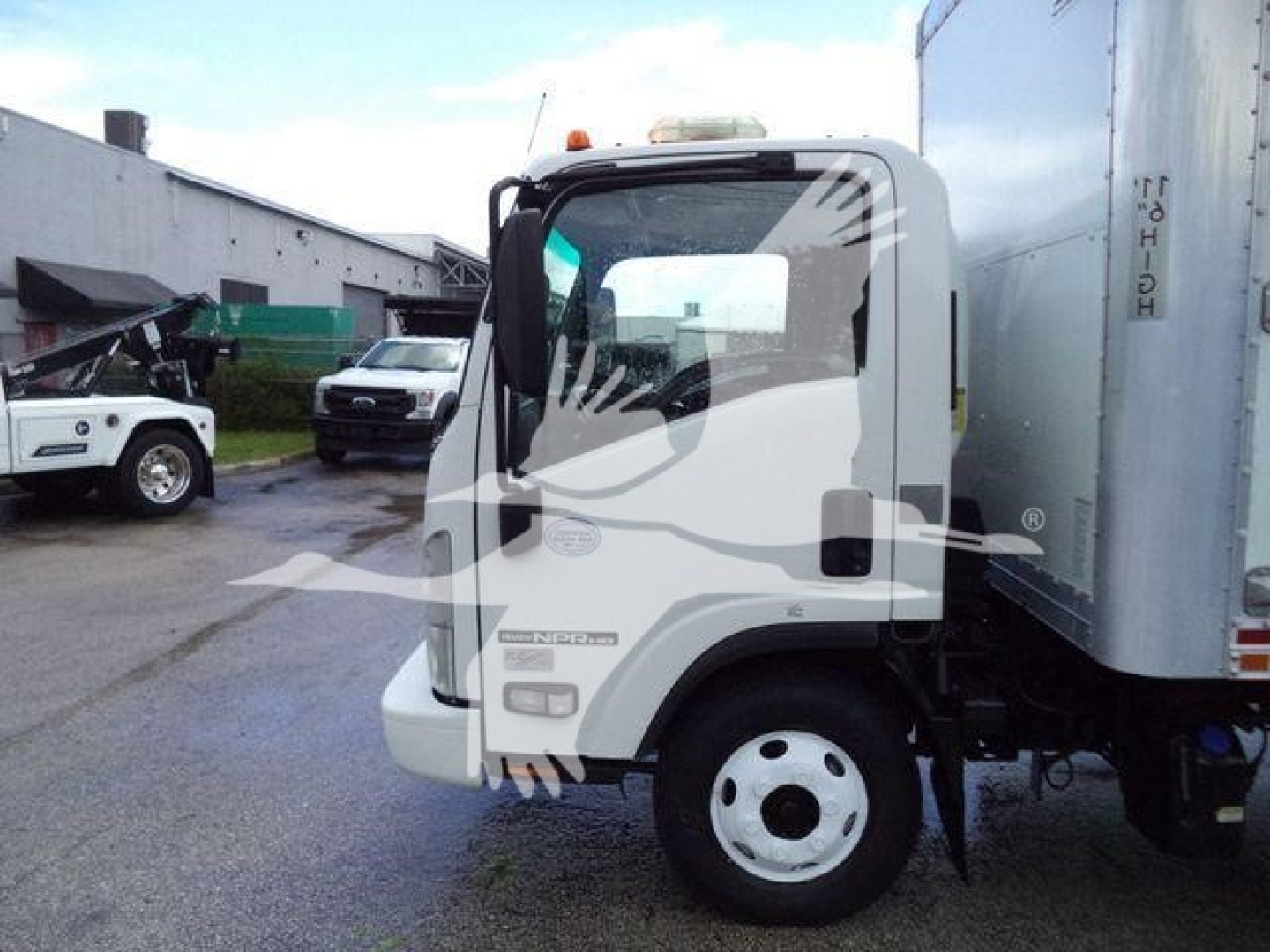 Isuzu NPR HD box truck cab side view showing front wheel and cargo box with decal text.