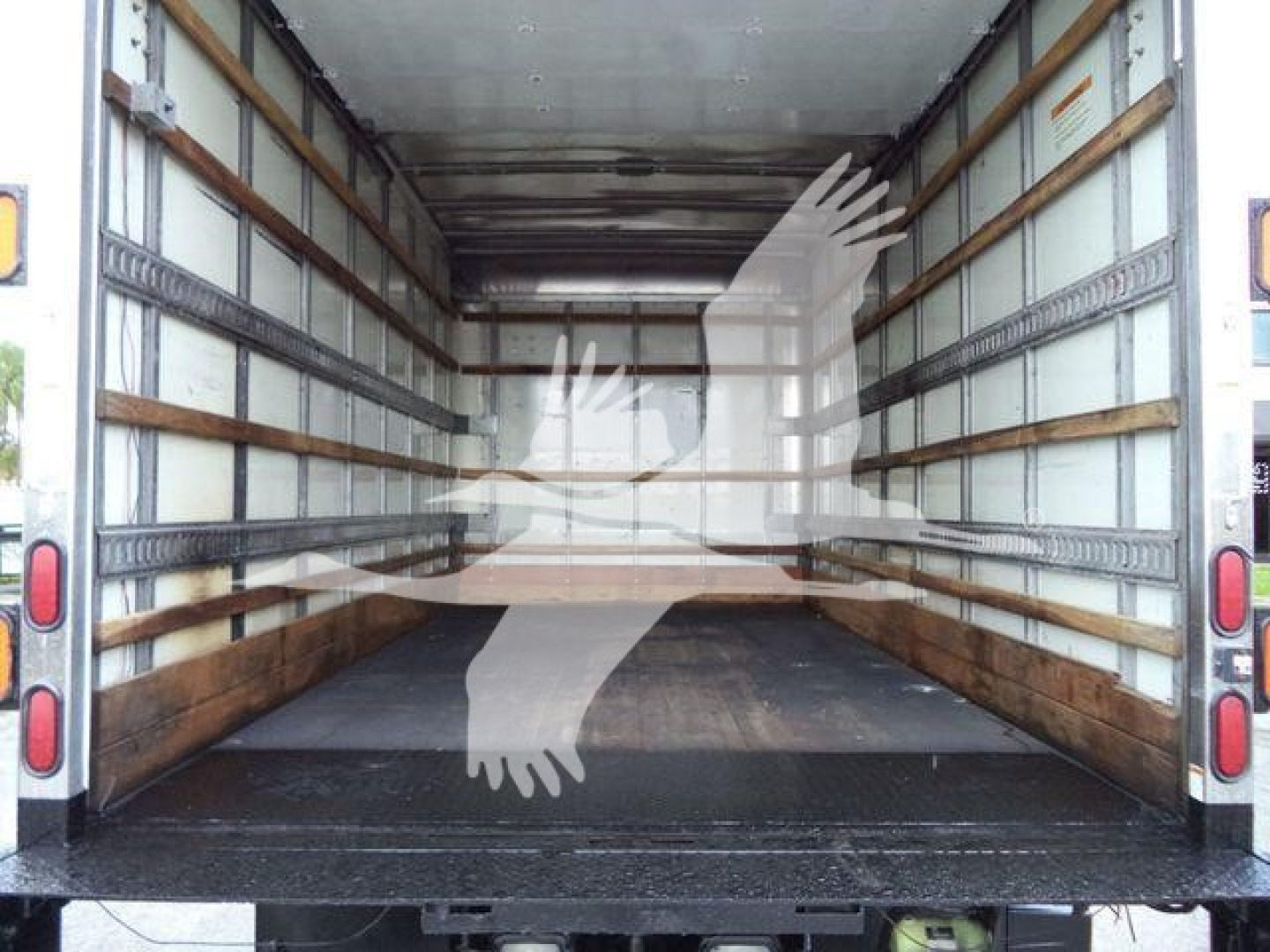 Isuzu NPR-HD box truck cargo area showing empty interior with metal track rails on walls and wooden floor; rear doors open; no cargo present.