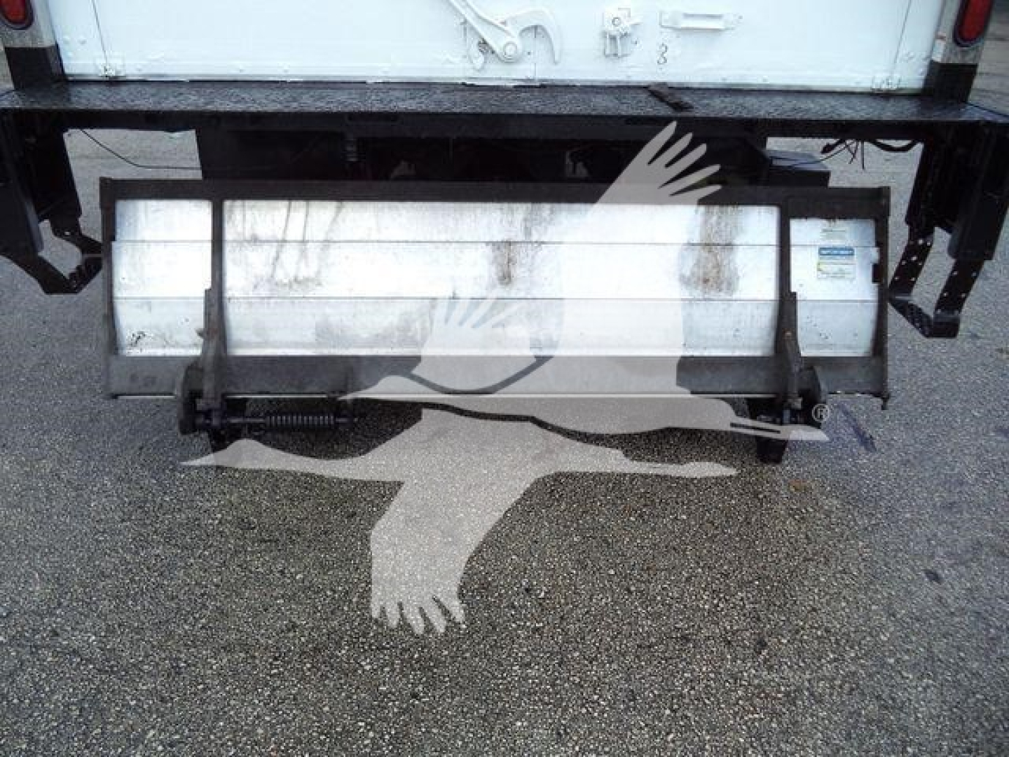 Isuzu NPR HD rear view showing a metal bumper/step with hydraulic components and a white cargo truck in the background.