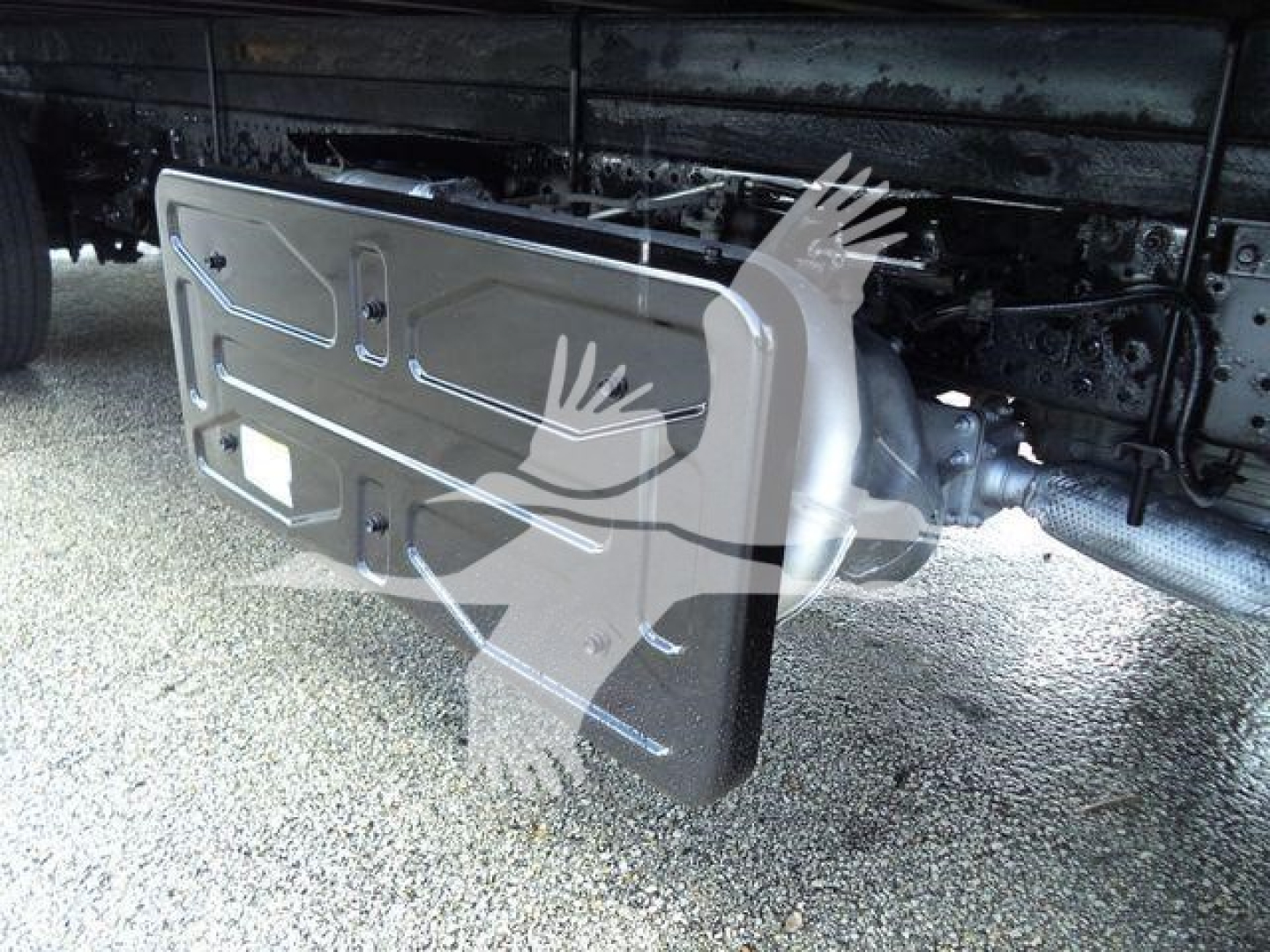 Isuzu NPR HD truck undercarriage showing a metallic skid plate/step bumper near the drive shaft and frame; partial view of chassis and exhaust.
