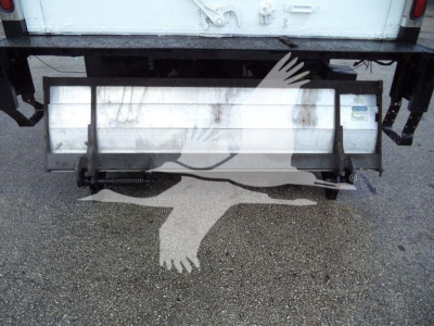 Isuzu NPR HD rear view showing a metal bumper/step with hydraulic components and a white cargo truck in the background.