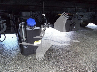 Underbody view of a 2015 Isuzu NPR HD chassis showing a blue engine coolant/def reservoir cap, hoses, and nearby metal brackets on a truck frame.