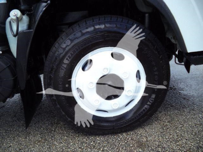 Isuzu NPR HD truck wheel and tire with white hubcap and surrounding fender, partial engine bay components visible.