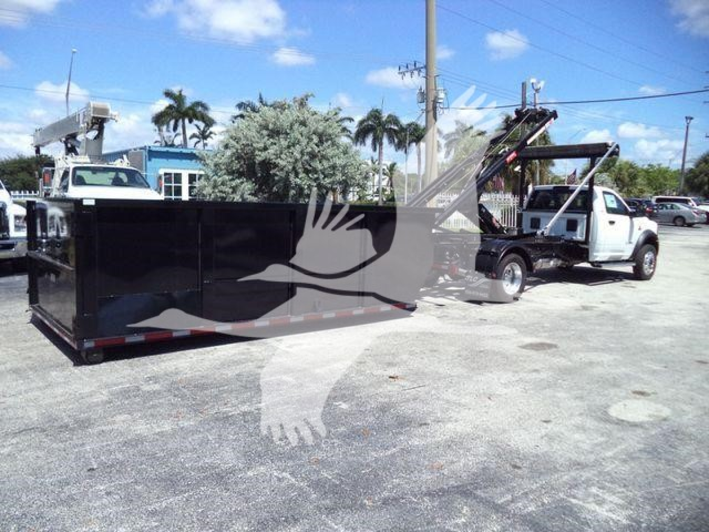 Truck bed with roll-off container and tow truck in background, 2024 Ram 5500 HD SLT listing stock DSL550014SNG4X4.