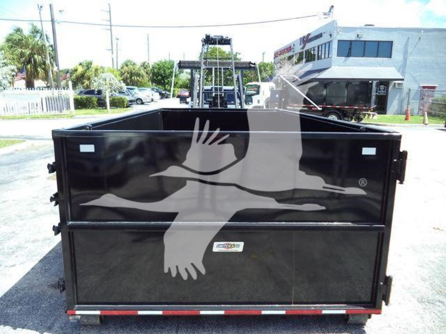 Ram 5500 dump truck bed showing black body with white logo on side and rear tailgate; roll-off truck equipment in background.