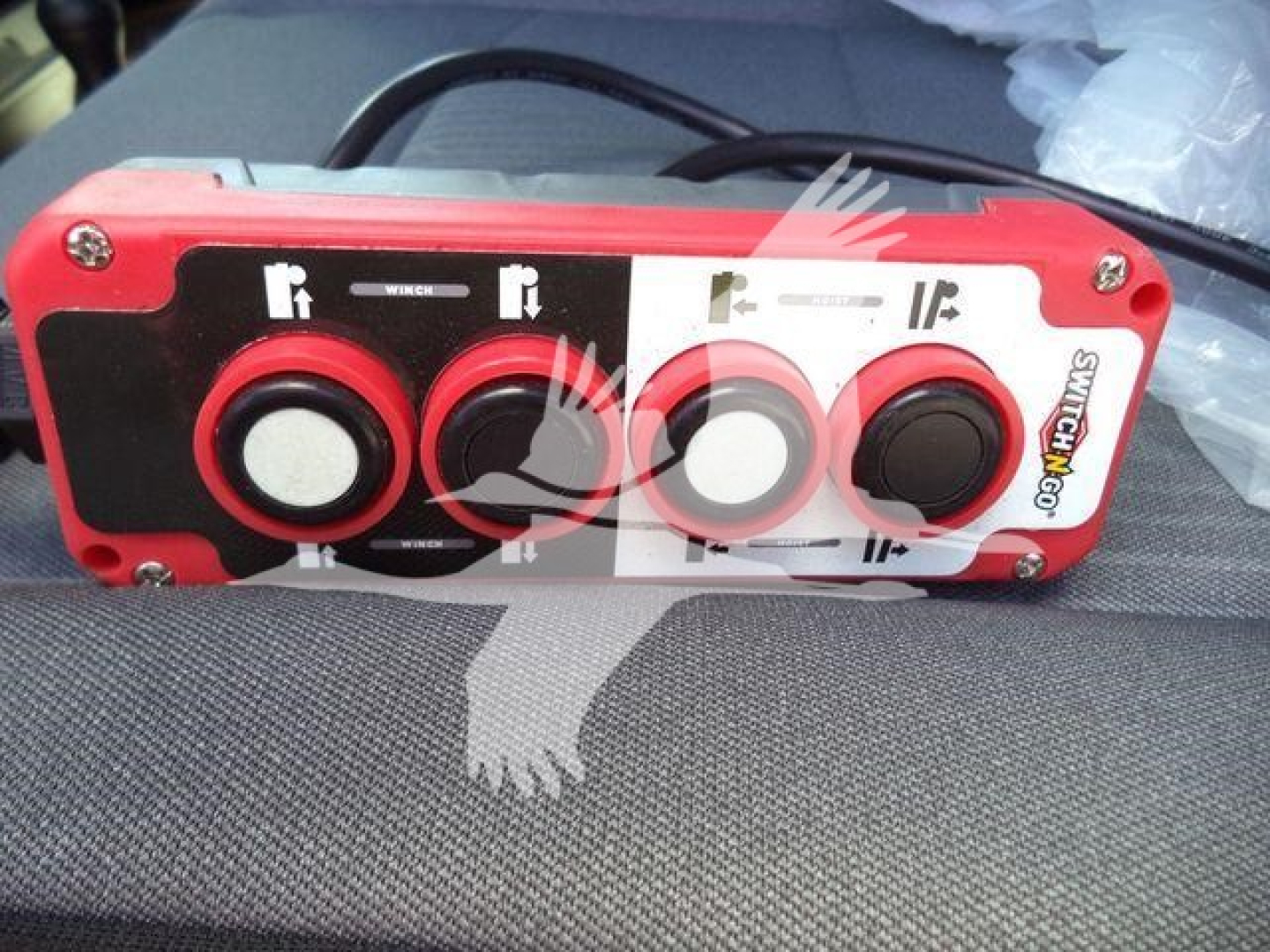 Panel view of a red control box with four circular knobs set in a black and white panel, wiring harness on top; labels and symbols around knobs.