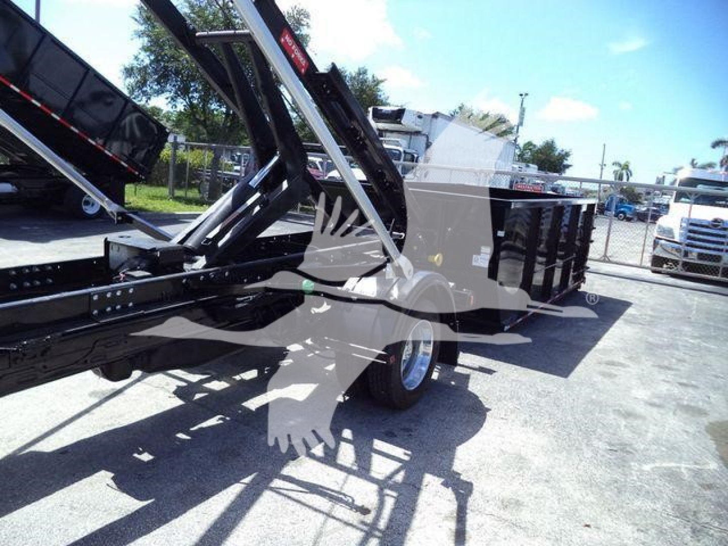 Ram 5500 dump bed truck with hydraulic lift and roll-off container in a lot.