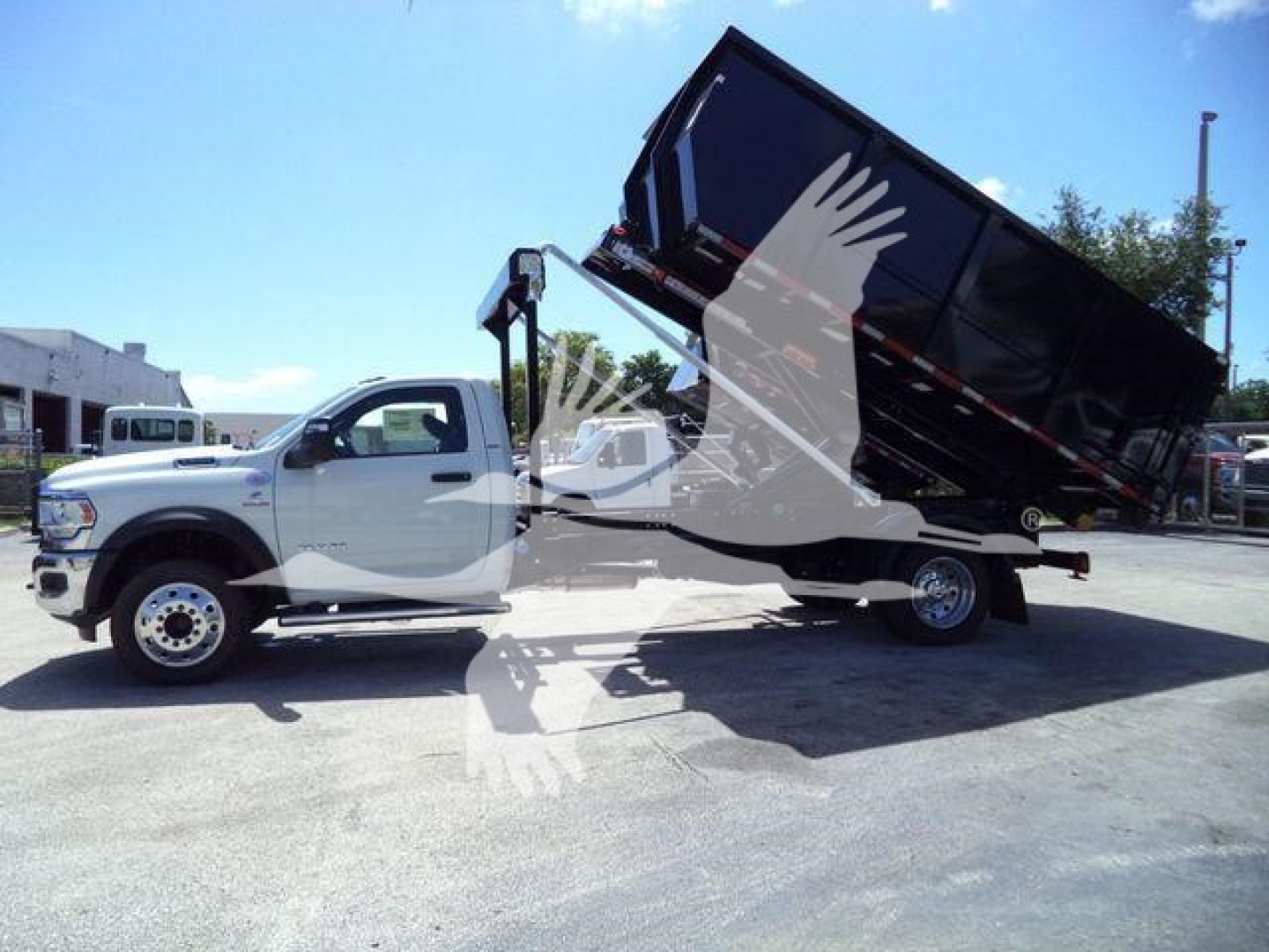 Ram 5500 dump truck in-service view with cargo bed raised, side profile visible, white cab and black bed, rollover truck chassis.