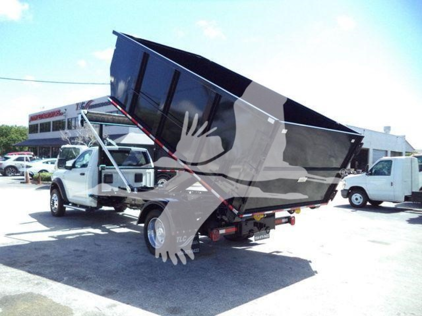 Ram 5500 dump truck in rollover position showing large dump bed raised on hydraulic cylinders; front cab visible, dealership backdrop.
