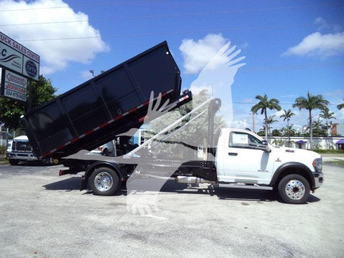Ram 5500 dump truck side view with raised black dump bed on a white cab chassis, in a dealership lot.