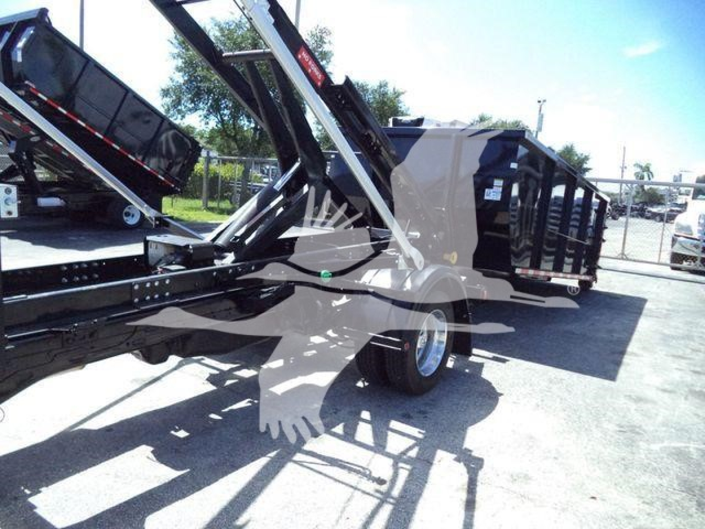 Ram 5500 HD SLT roll-off truck trailer showing loading mechanism and dumped bed with hydraulic arms, black chassis, and dual rear wheels.