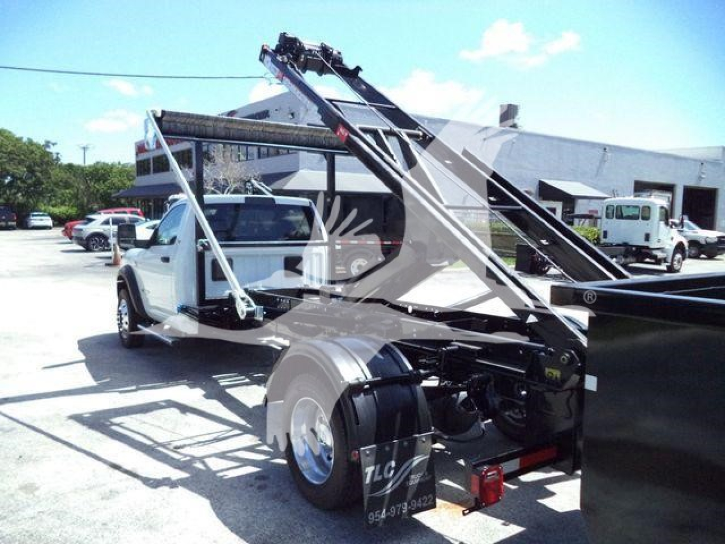 Ram 5500 HD SLT rolloff truck in white with loading arm and metal framework, side view showing rear wheels and towing hitch.