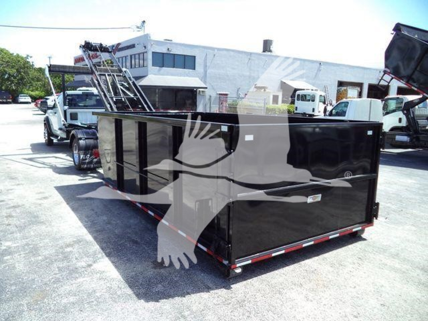 Roll-off truck body in black with a white handprint graphic, rear doors visible, trailer hitch, and industrial building in background.