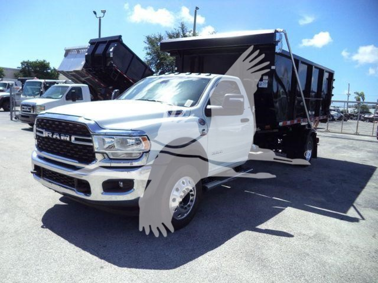 Ram 5500 HD SLT truck with dump bed, front grille, headlights, bumper, and side mirrors visible; white vehicle with black dump body and raised bed on a lot.