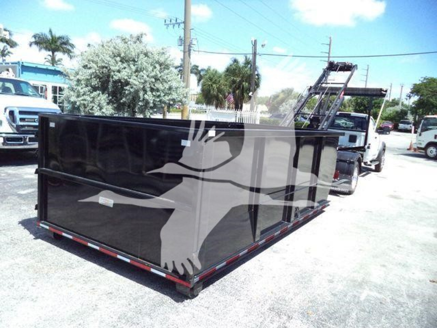 Ram 5500 dump-style roll-off dumpster body in black with deer head logo on side showing stock trailer and trucks in background.