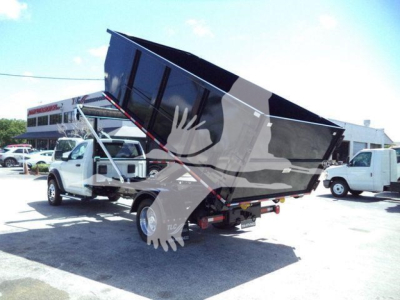 Ram 5500 dump truck in rollover position showing large dump bed raised on hydraulic cylinders; front cab visible, dealership backdrop.