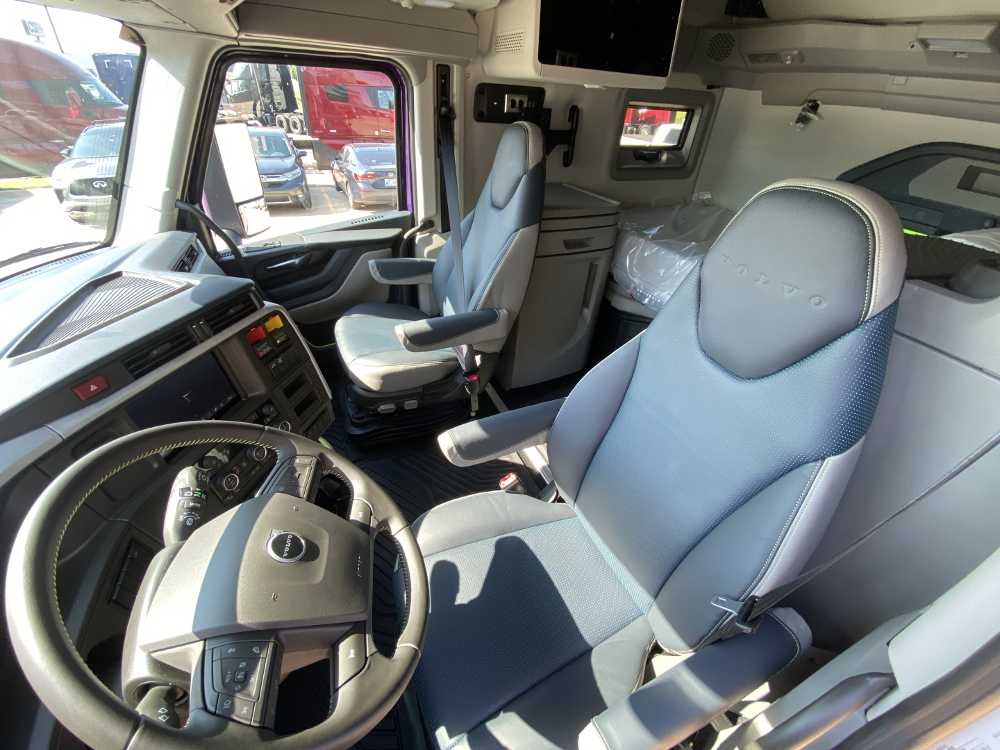 Volvo VNL64T860 truck cab interior showing steering wheel, driver seat, and passenger seat with dashboard controls and overhead storage.