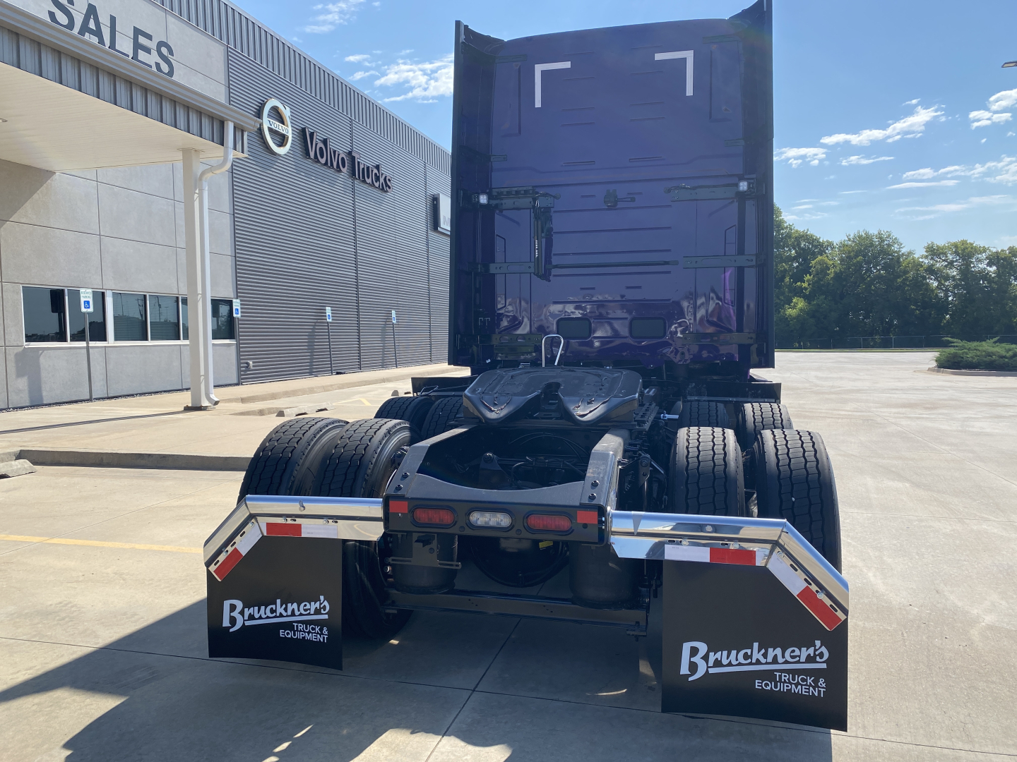 Volvo VNL64T860 truck tractor rear view showing fifth wheel and dual rear axles with mud flaps reading Bruckner's Truck & Equipment; dealership building in background.