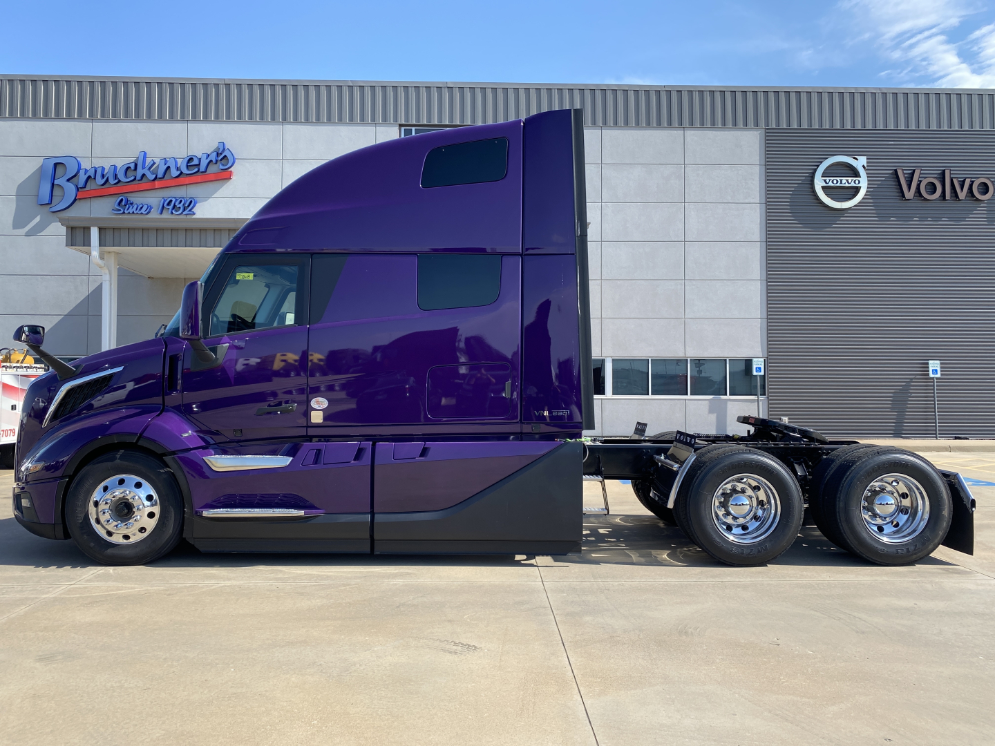 Volvo VNL64T860 sleeper cab semi-truck in purple finish, side view, 6x4 configuration parked in front of a Volvo dealership.