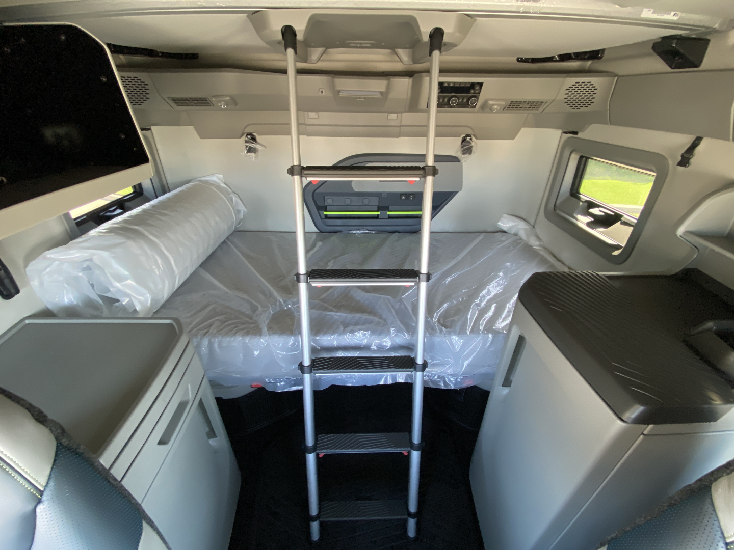 Volvo VNL64T860 sleeper cab interior with ladder to bunk, plastic-wrapped bed, overhead storage, and compact kitchenette.