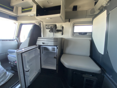 Volvo VNL64T860 cab interior showing open mini-fridge, storage drawers, overhead compartments, and passenger bench seating.