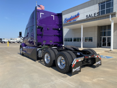 Volvo VNL64T860 tractor in purple exterior, rear view showing dual rear axles and mud flaps, parked outside dealership with 'Sales' building in background