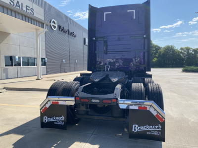 Volvo VNL64T860 truck tractor rear view showing fifth wheel and dual rear axles with mud flaps reading Bruckner's Truck & Equipment; dealership building in background.