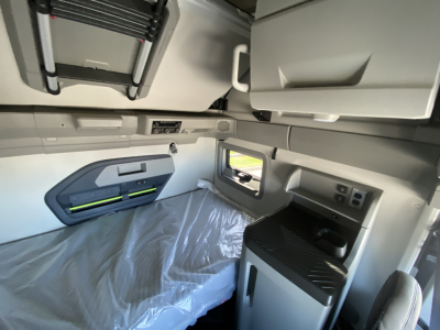 Cab interior of a Volvo VNL64T860 sleeper showing upper storage cabinets and side panels with a window and control panel.